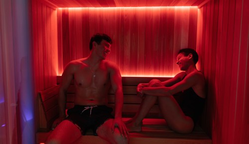 A candid shot depicting a fitness couple engaging in a workout recovery in an infrared sauna, surrounded by the warmth of wooden decor.