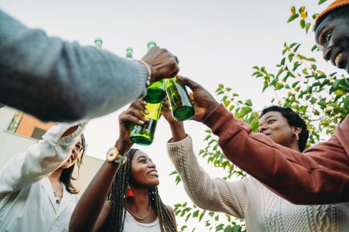 a group of people in their backyard clinking their green beer bottles together in the middle of the photo, wondering is beer good for you