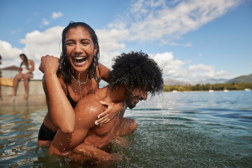 couple playing around in the ocean on their summer vacation as part of their summer bucket list based on their zodiac sign