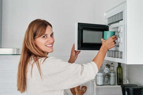 Young woman in the kitchen putting a cup in the microwave to heat it up.