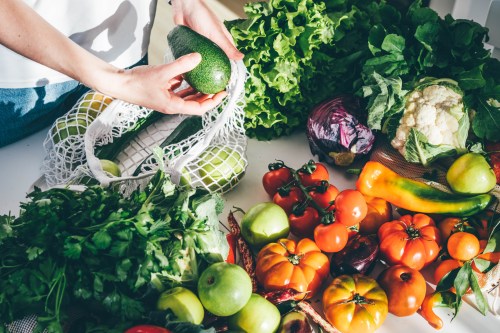 woman taking fresh organic vegetables out of a mesh bag on a table