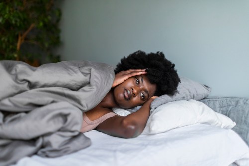 Depressed frowning young adult black woman with headache lying in bed