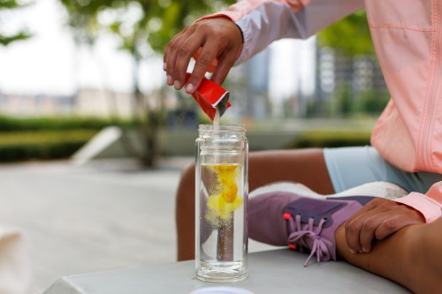 young woman in running gear pouring electrolyte powder into a clear bottle filled with water.