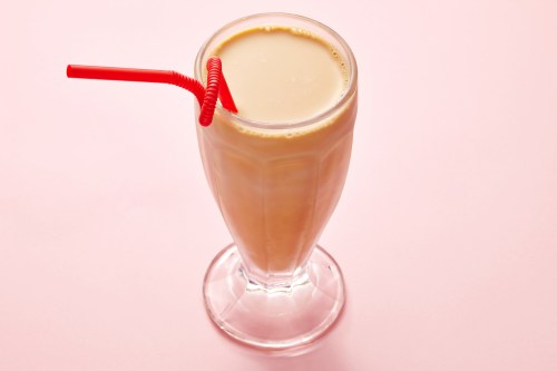 milkshake in a clear glass with straw on pink background