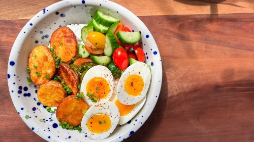 a blue speckled bowl filled with cottage cheese, potatoes, veggies, and eggs sits on a wood surface.