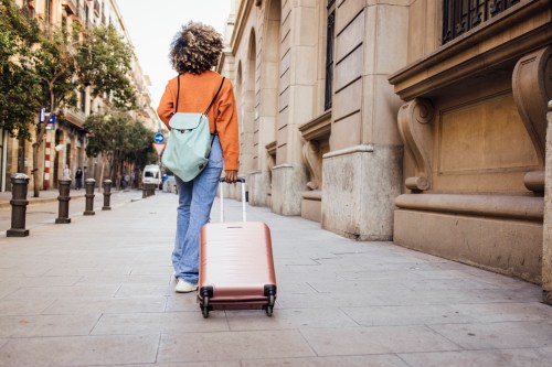 close up of person walking outside with their suitcase and a backpack walking through the streets of an international city, partaking in medical tourism
